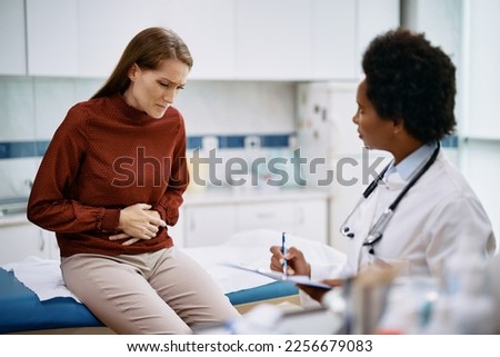 Female patient holding her abdomen in pain while talking to her doctor at medica clinic. Royalty-Free Stock Photo #2256679083