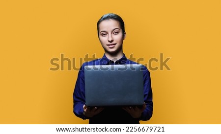 Teenage female student with laptop on yellow background