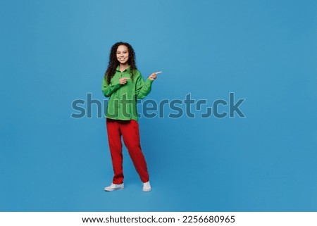 Full body young woman of African American ethnicity 20s she wear green shirt pointing index finger aside indicate on workspace area copy space mock up isolated on plain blue background studio portrait