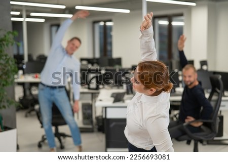 Three office workers warm up during a break. Employees do fitness exercises at the workplace. 