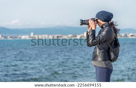 A young woman photographer takes photos or videos on the camera on a background of a sea landscape.