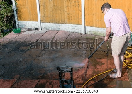 A man using a power pressure washer to clean a dirty stained patio with pressurised water jet
