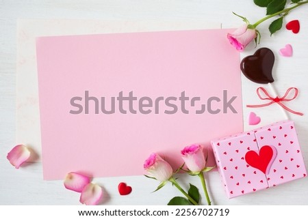 White wooden background with pink paper for congratulations text, gift box, chocolate candy, hearts, roses and petals. Postcard for Valentine's Day, wedding, Mother's Day and other holidays.