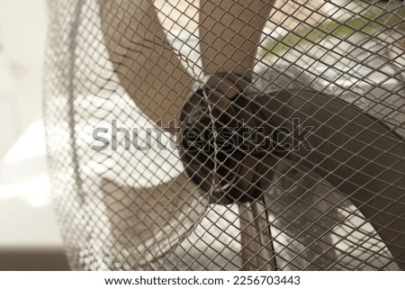 white fan with gray blades on the background of a window through a metal mesh close-up