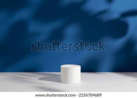 Empty white round podium and deep shadows on dark blue background. Showcase for product presentation. Pedestal for beauty cosmetic advertising. Minimal still life. Front view. Royalty-Free Stock Photo #2256704689