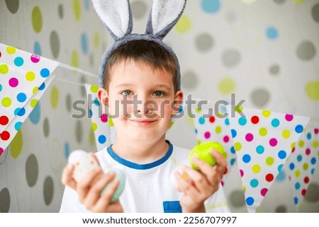 Cute boy with bunny ears holding Easter eggs.