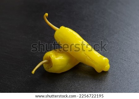 Two pickled yellow peppers, pepperoncini or friggitelli on black slate background. Hot pepper marinated, brined. Traditional Italian and greek cuisine, ingredient for salad, pasta, sauce. Royalty-Free Stock Photo #2256722195
