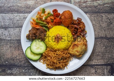 Indonesian traditional food, nasi kuning  yellow turmeric rice served with beef rendang, fried chicken, vegetables, spicy eggs, noodles  and tempeh Royalty-Free Stock Photo #2256727663