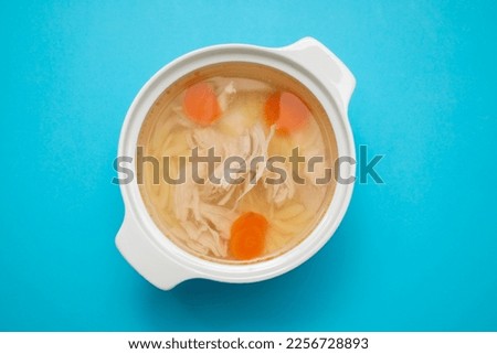 bowl of chicken broth with chicken and carrot in blue paper
