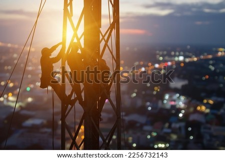 Silhouette workers on construction crews to work on high ground heavy industry and connection development, distribution electrical concept. Extension of high-voltage towers on blur city background. Royalty-Free Stock Photo #2256732143
