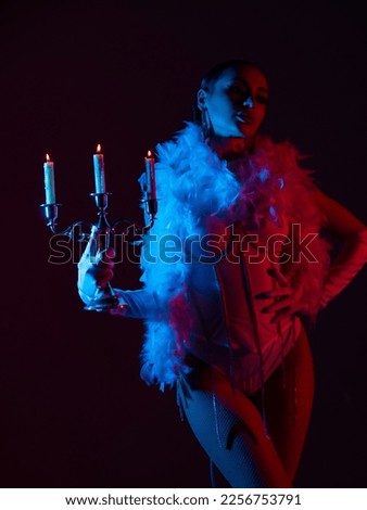 Brunette in a white dance bodysuit with a bright evening make-up with a white boa with a candelabra and three burning candles with colored red-blue lighting