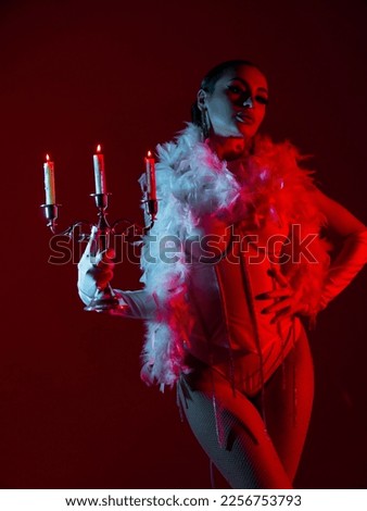 Brunette in a white dance bodysuit with a bright evening make-up with a white boa with a candelabra and three burning candles with colored red-blue lighting