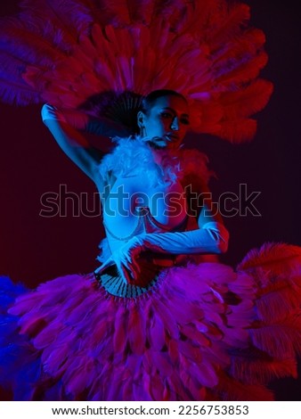 Brunette in a white dance bodysuit with a bright evening make-up with a white boa with large fans with colored red and blue lighting