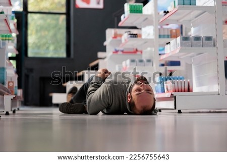 Young caucasian man having epilepsy attack, lying unconscious on floor in medical retail store. Pharmacy store customer fainting, suffering from neurological disease seizure Royalty-Free Stock Photo #2256755643