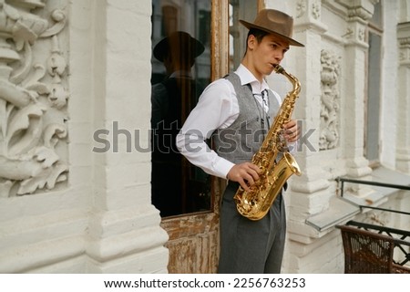 Young male musician practicing saxophone in balcony at home Royalty-Free Stock Photo #2256763253