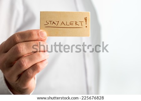 Close up Simple Stay Alert Concept Design with Businessman Showing Small Wooden Sign with Underlined Stay Alert Texts over White Shirt.