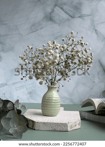 Baby breath flower in the green vase, on the wooden board, with eucalyptus and books at side, and green textured backdrop