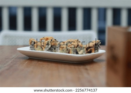 Japanese food called Volcano Salmon Roll Sushi. Served warm on a white rectangular plate on the table with a slanted cut.