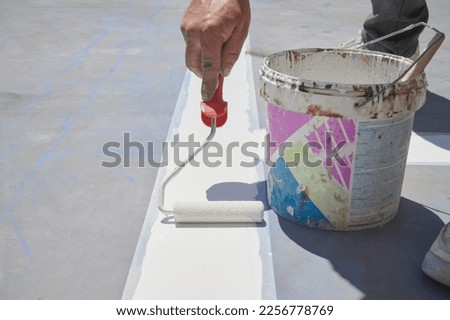 Professional painter at work. Unrecognizable young man uses a paint roller to apply special acrylic paint for road marking on asphalt.