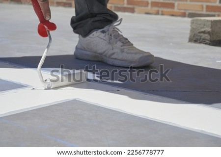Professional painter at work. Unrecognizable young man uses a paint roller to apply special acrylic paint for road marking on asphalt.