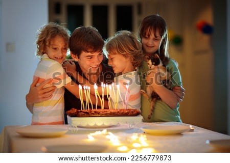 Teenager boy birthday with family and younger brother and sister. Siblings blow candles at party cake. Family love. Kids hug and kiss big brother. Children bonding.