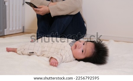 A picture of a parent who is tired of childcare looking at a smartphone and escaping from childcare. Infant babies are left lying nearby