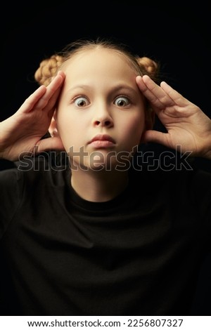 Portrait of a beautiful surprised girl in a black t-shirt on a black studio background. Children, emotions. Psychological picture.