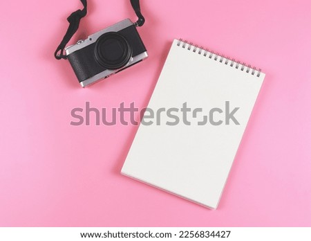 Top view or flat lay of blank page opened notebook and camera on pink background.
