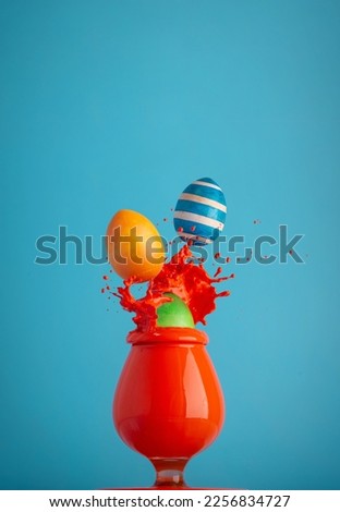 Multicolored eggs with splashes fall into the paint. A bright Easter card. A picture in the style of minimalism.