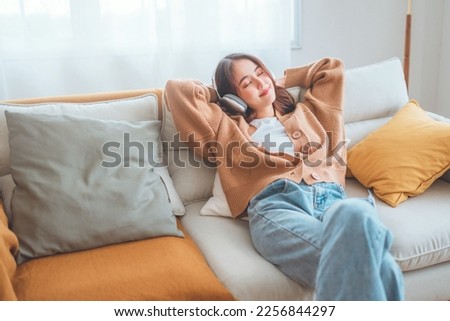 Happy asian woman listening to music from mobile phone while sitting on the the sofa at homes, Smiling girl relaxing with headphones in morning, Time to relax. copy space. Royalty-Free Stock Photo #2256844297