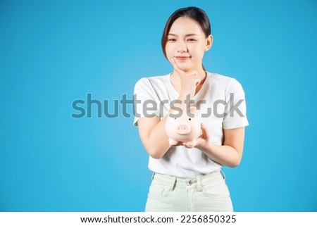 Photo of young Asian woman holding piggy bank on background