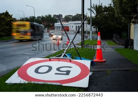 50km speed limit sign blown over by the wind. Out-of-focus cars travelling on the road. Auckland after the storm.
