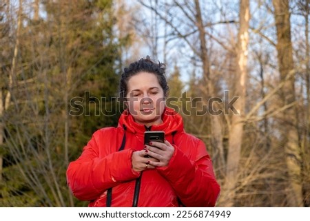 A girl in a red jacket looks at the background of the forest on her phone