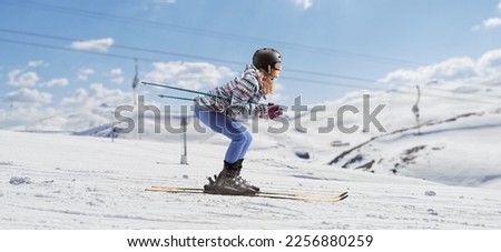 Full length profile shot of a young woman skiing under a ski lift