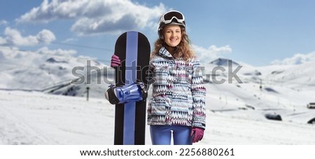 Young female with goggles and helmet posing on a mountain and holding a snowboard