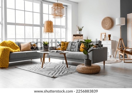 Beautiful interior of living room with cozy grey sofas, table and houseplants near window
