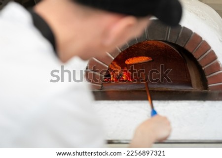 Italian pizza is cooked in a wood-burning oven. The cook puts the pizza in the oven on a shovel