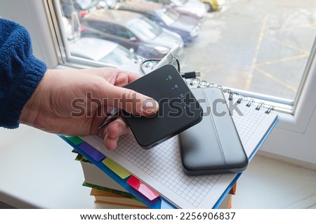 Person holds Portable 3g 4g mobile wireless internet router with power bank on window at home. To connect to the internet for online learning and working during a blackout, power outage. Royalty-Free Stock Photo #2256906837