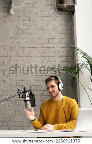 Man podcaster influencer blogger smiling while broadcasting his live audio podcast in studio using headphones, laptop and headphones. Male radio host making podcast or interview