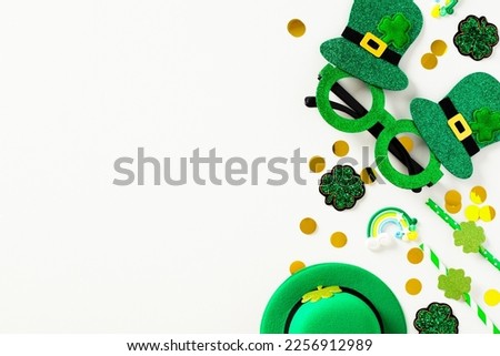 St Patrick's Day flat lay composition with green party glasses, leprechauns hat, drinking straws, confetti, shamrock clover leaves on white background.