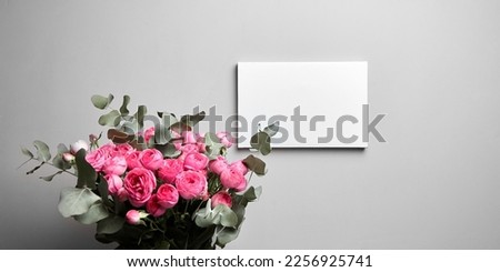 White canvas mockup hanging on grey wall and bouquet of pink roses with eucalyptus leaves. Empty blank canvas, interior decor