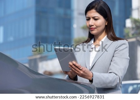 Businesswoman using digital tablet leaning on car in city.