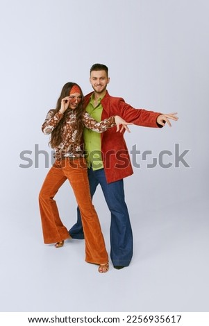 Beautiful young girl and handsome man in bright retro clothes, disco dancers posing isolated over grey studio background. 70s fashion, hobby, creativity, hippie lifestyle, American culture