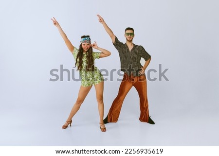 Peace. Stylish young man and woman in fashionable retro outfits dancing disco dance, posing isolated over grey studio background. 70s fashion, hobby, creativity, hippie lifestyle, American culture Royalty-Free Stock Photo #2256935619