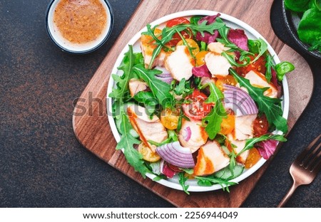 Grilled salmon fish salad with tomato, cucumber, arugula, radicchio, red onion and lettuce with lemon and sesame seeds. Brown table background, top view
