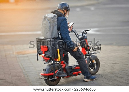 Online delivery service, delivering food with e-scooter. Courier rides electric moto bike, deliver food orders to customers. Boy in helmet ride electric scooter with thermal box, fast food delivery. Royalty-Free Stock Photo #2256946655