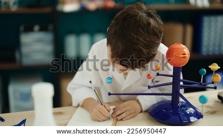 Adorable hispanic boy astronomer student make planetary work writing on notebook at laboratory classroom