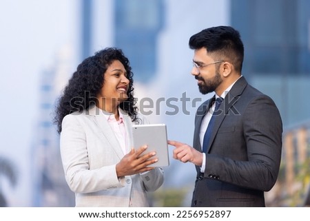 Indian businessman and businesswoman using digital tablet on city street