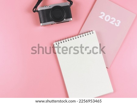 Top view or flat lay of blank paper notebook on pink diary 2023 with camera on pink background.