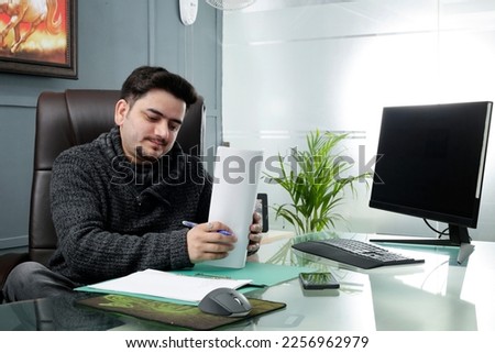A young businessman is sitting in office and holding some paper in hands.